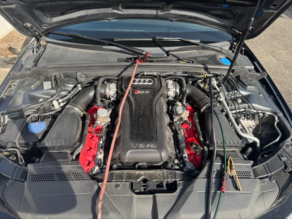 Moteur Audi RS 4 V8 FSI avec couvercles rouges, câbles de démarrage connectés. Le compartiment moteur est ouvert en plein jour.